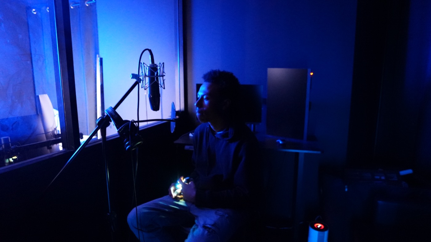 Artist seated at the mic in the recording booth
