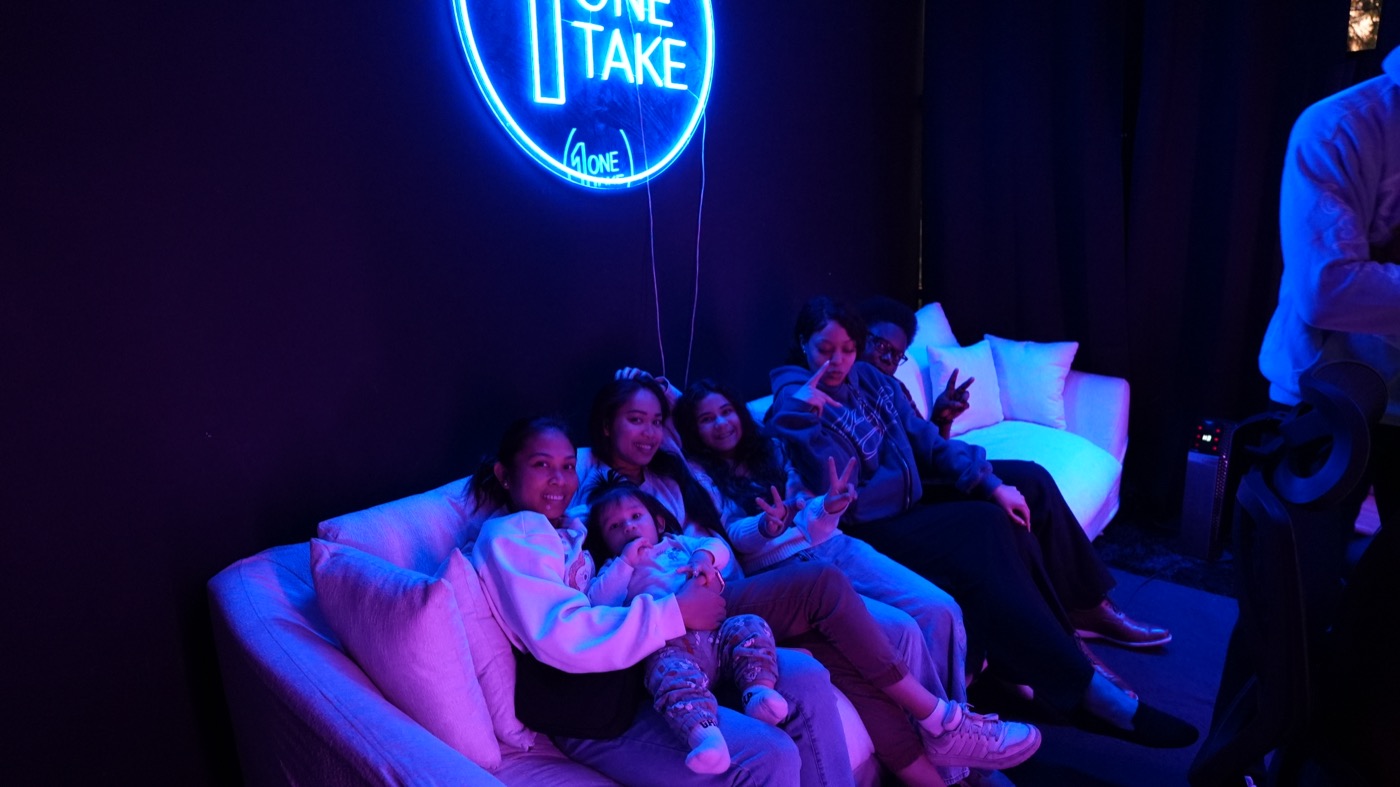 Friends and family on the lounge couch beneath the neon sign