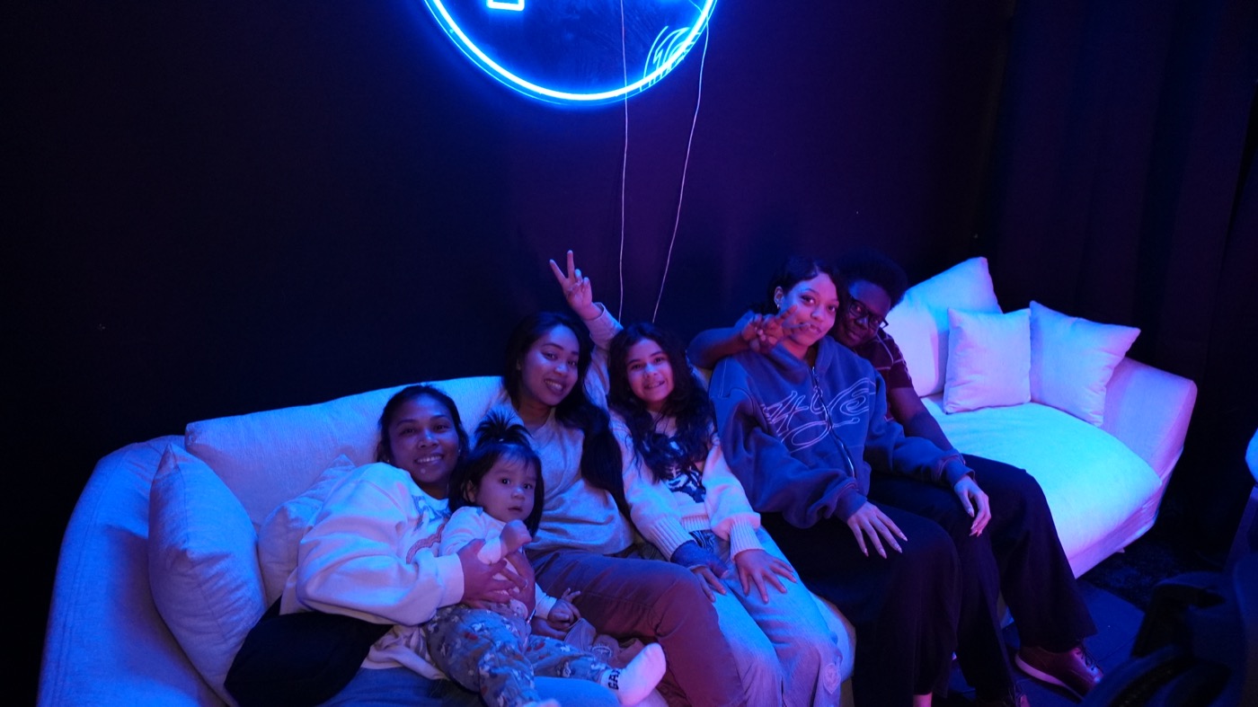 Group hanging out on the studio couch under the neon sign