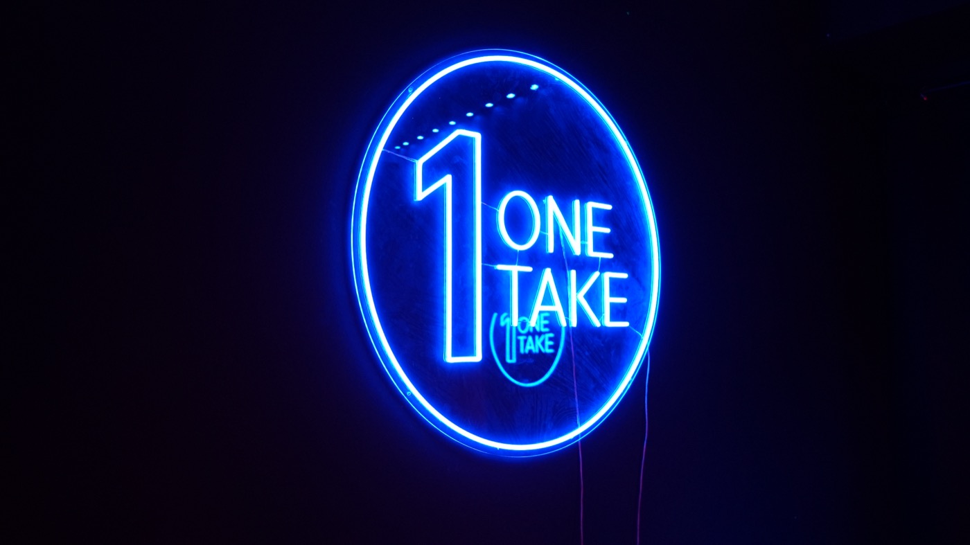 The One Take neon sign glowing blue on the studio wall