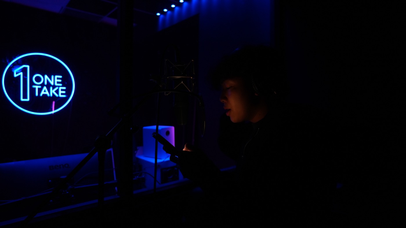 Artist at the mic lit only by the neon sign