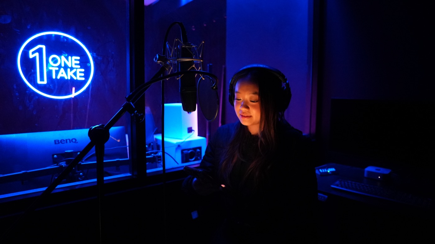 Artist tracking vocals in headphones beside the neon sign