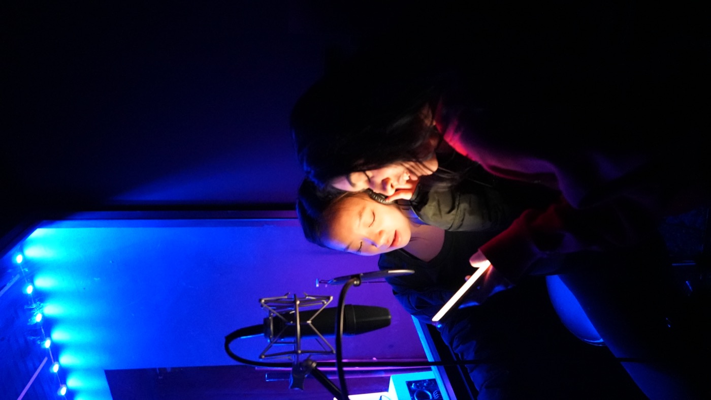 Two artists reading lyrics off a phone in the booth