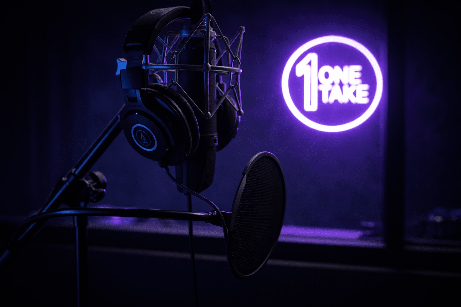 Neumann microphone and headphones in front of the One Take neon sign